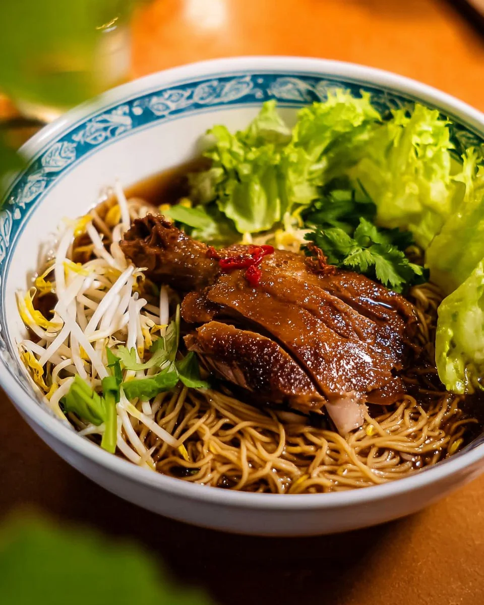 A bowl of Thai Duck Noodle Soup garnished with herbs and spices.